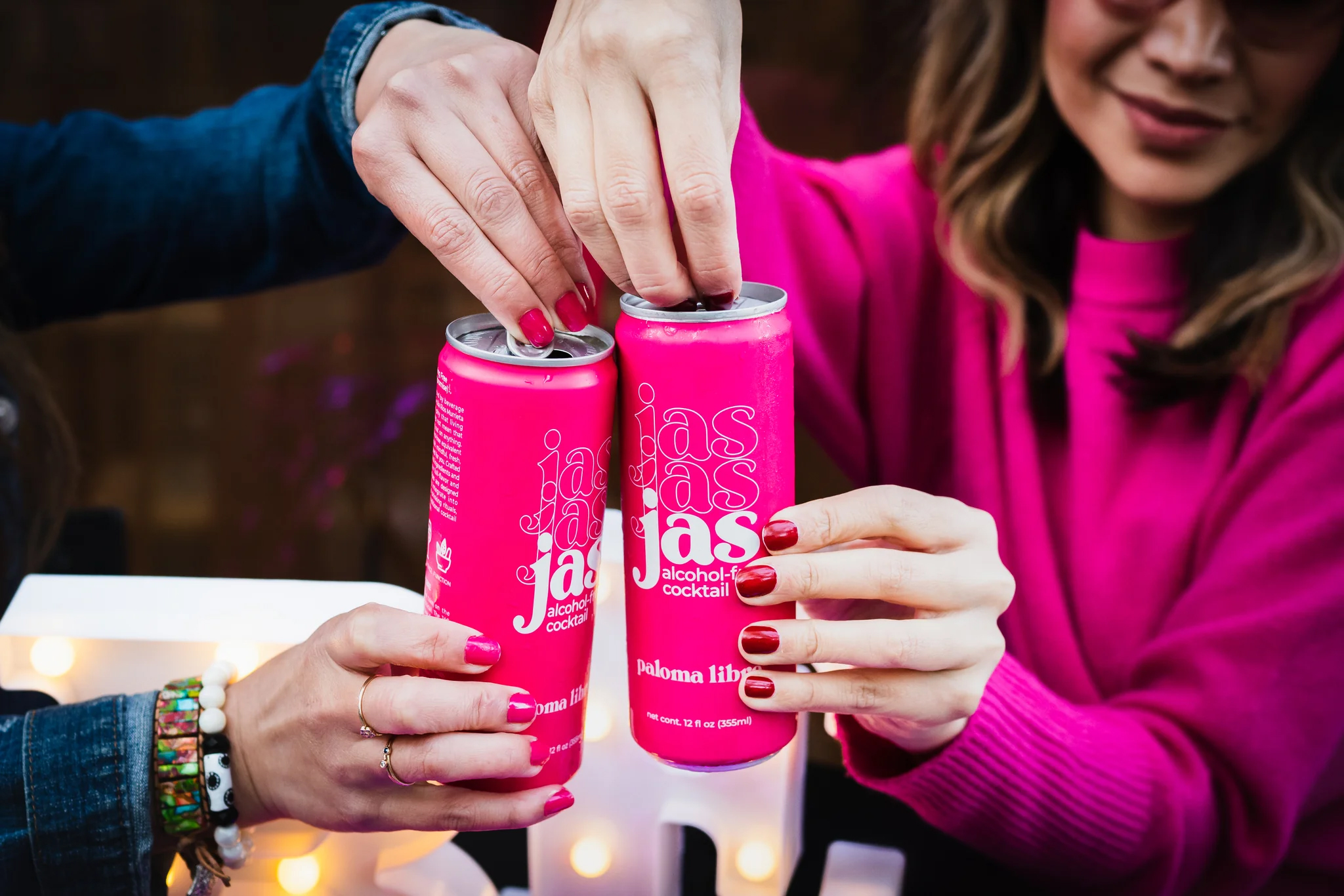 A close up of JAS drinks in pink cans being opened by two women.