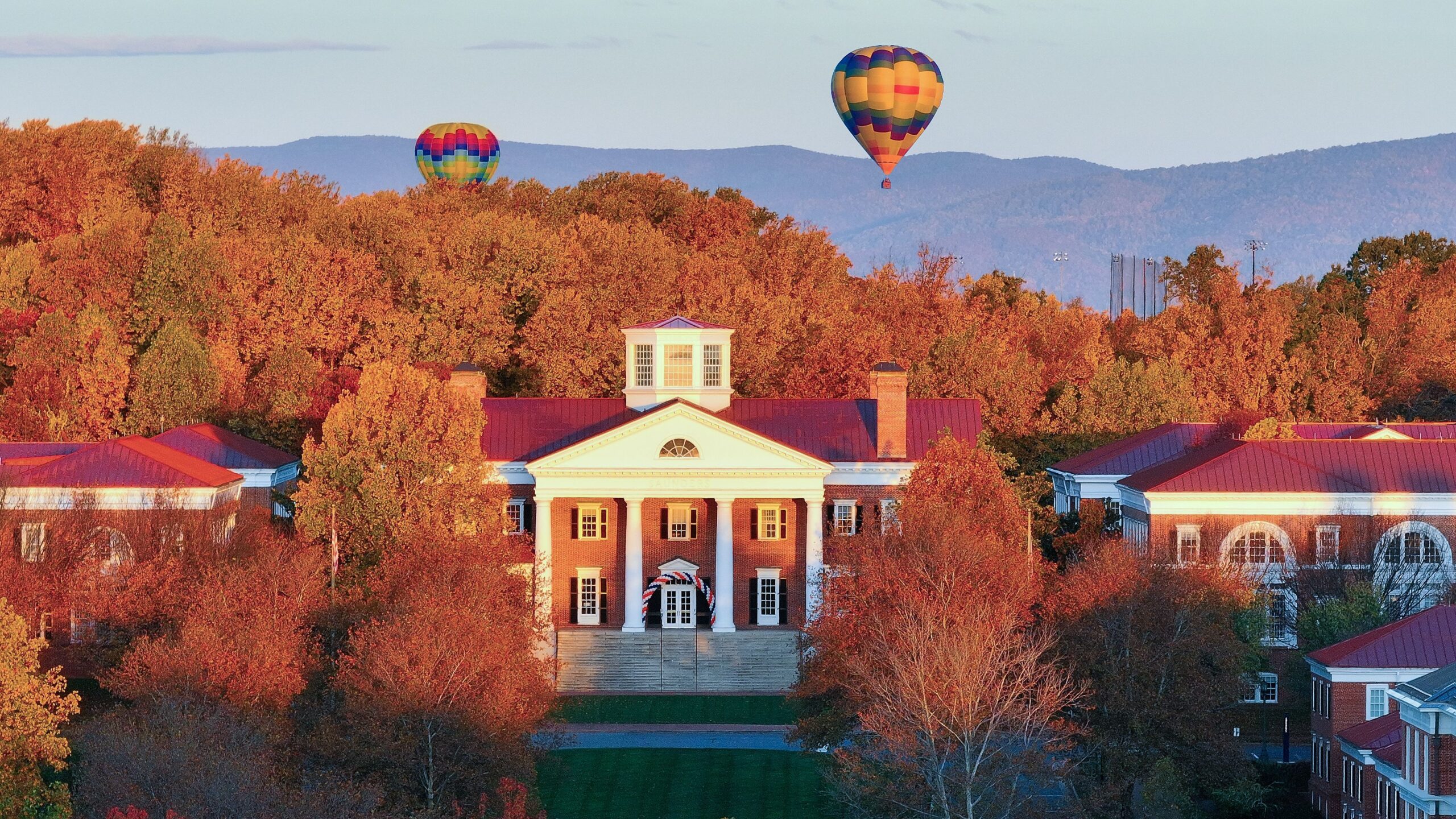 Aerial photo of Darden Grounds in the fall, with orange foliage and hot air balloons in the background.