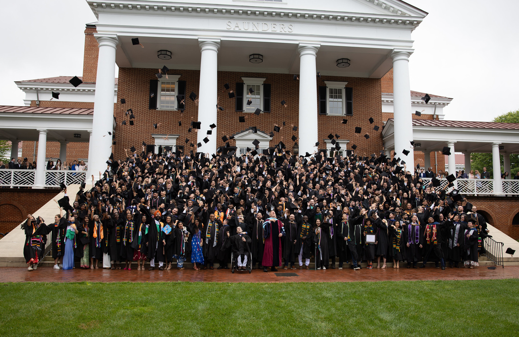 A group shot of the Darden graduates throwing their hats on the steps of Saunders Hall.