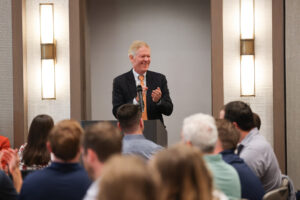 Darden Dean Scott Beardsley speaking at a podium in front of a crowd.